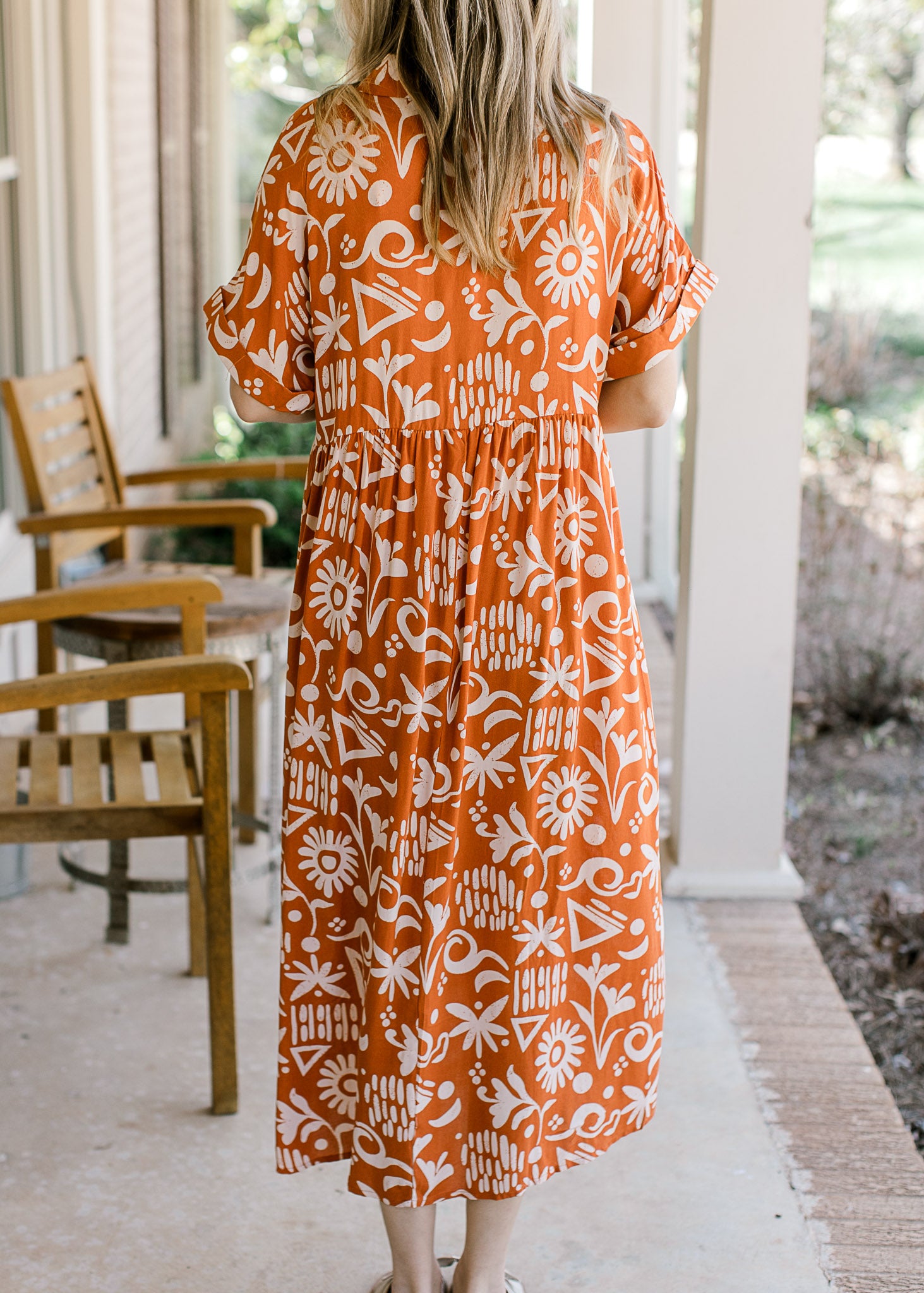 Back view of Model wearing an orange button up midi with a cream print and short sleeves with cuffs.
