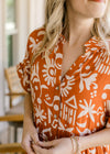Close up of v-neck, buttons and short sleeves on an orange midi with a cream pattern.