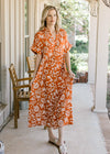 Model wearing an orange lightweight dress with a cream print, buttons and short sleeves.