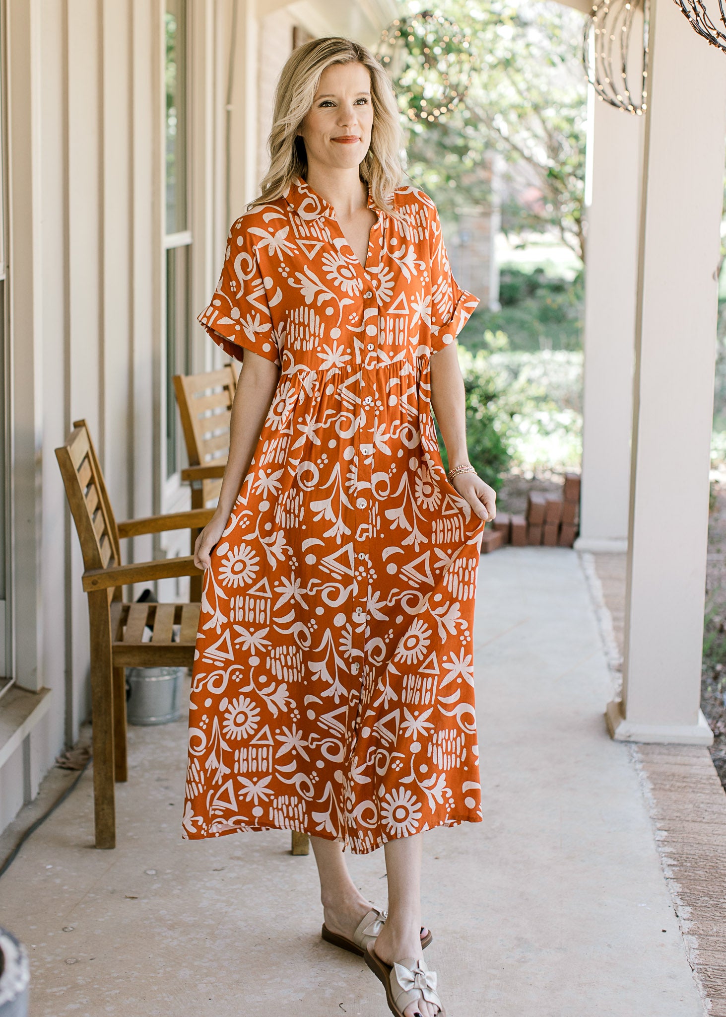 Model wearing an orange lightweight dress with a cream print, buttons and short sleeves.