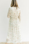 Back view of Model wearing a cream dress with a tan floral pattern, elastic waist and sheer sleeves.