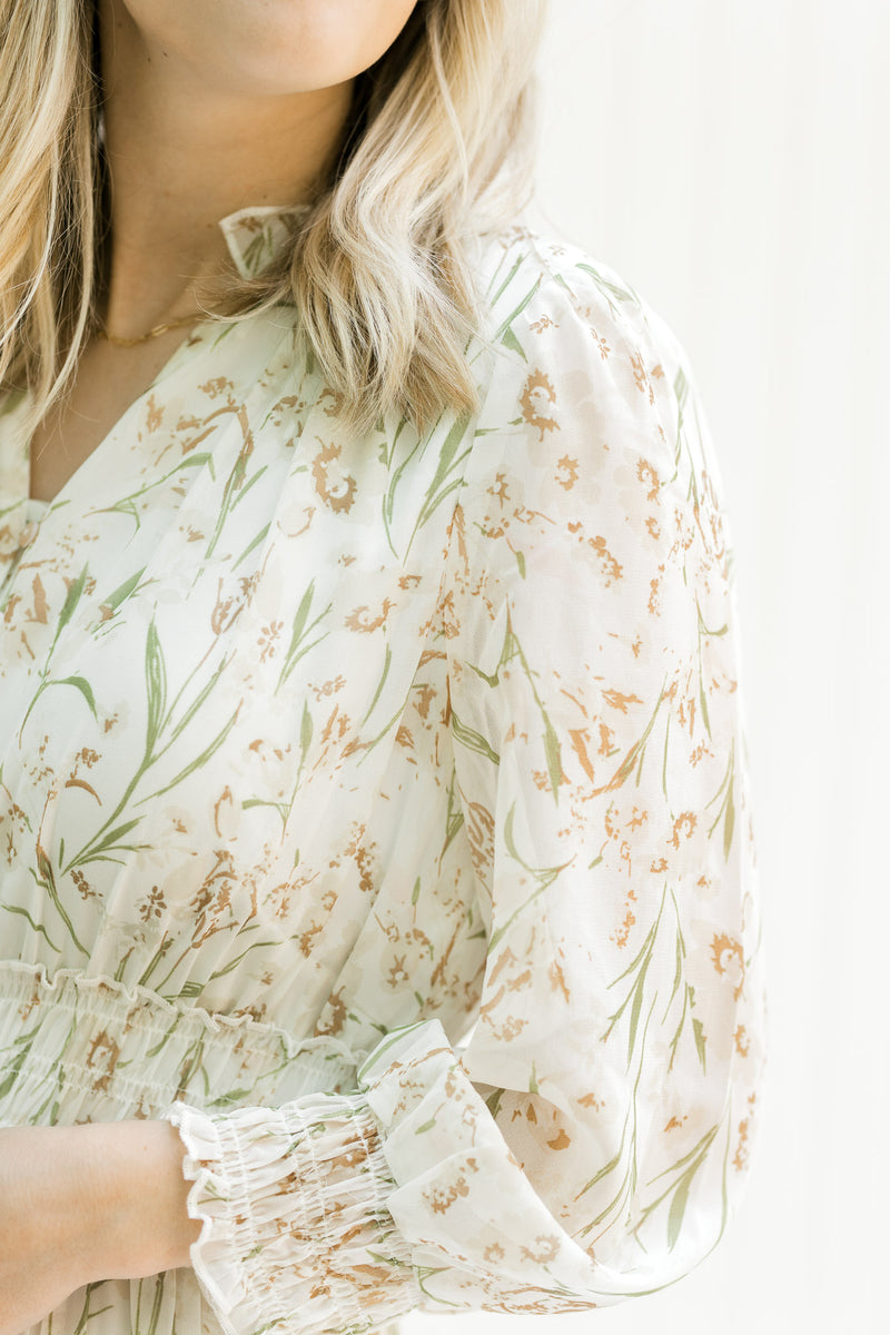 Close up view of sheer long sleeves with elastic cuff and ruffle at neck on a cream floral dress. 