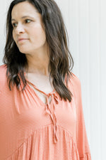 Close up of dotted pattern and v-neck with a tie on a salmon colored above the knee dress. 