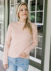 Model wearing jeans with a blush sweater with ribbed material, mock neck and long sleeves. 