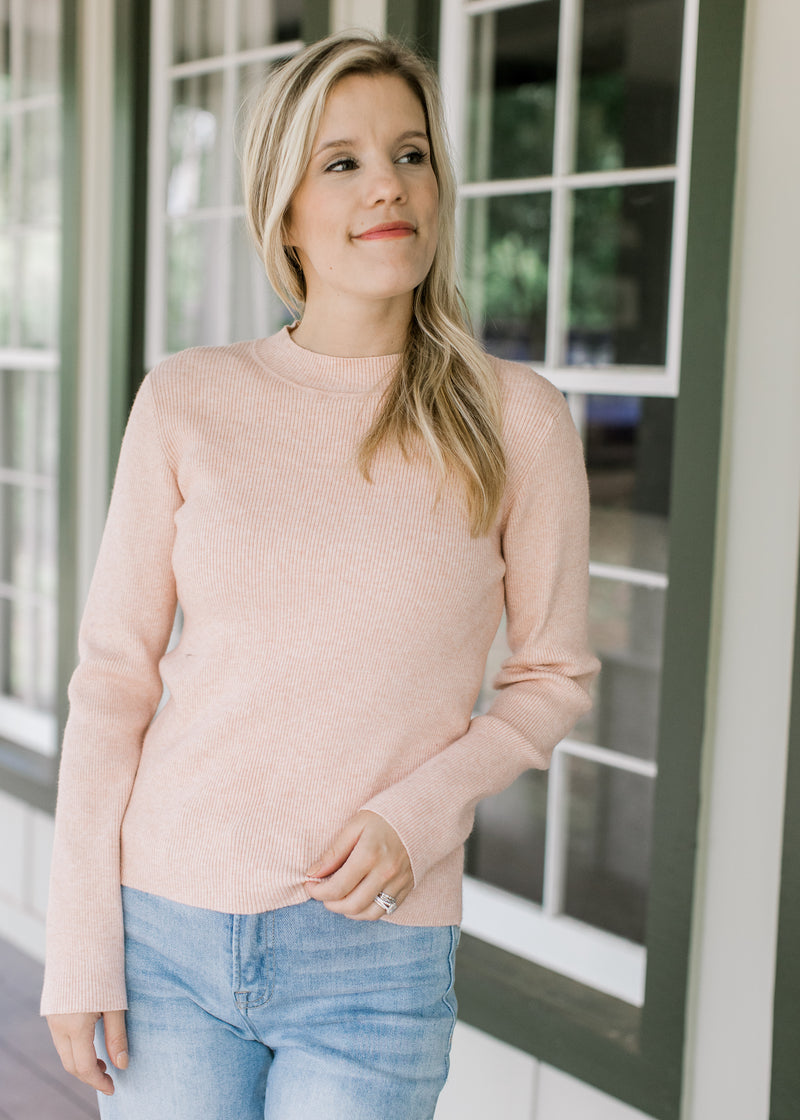 Model wearing jeans with a blush sweater with ribbed material, mock neck and long sleeves. 