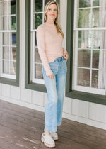 Model wearing jeans, mules and a blush sweater with ribbed material, mock neck and long sleeves. 