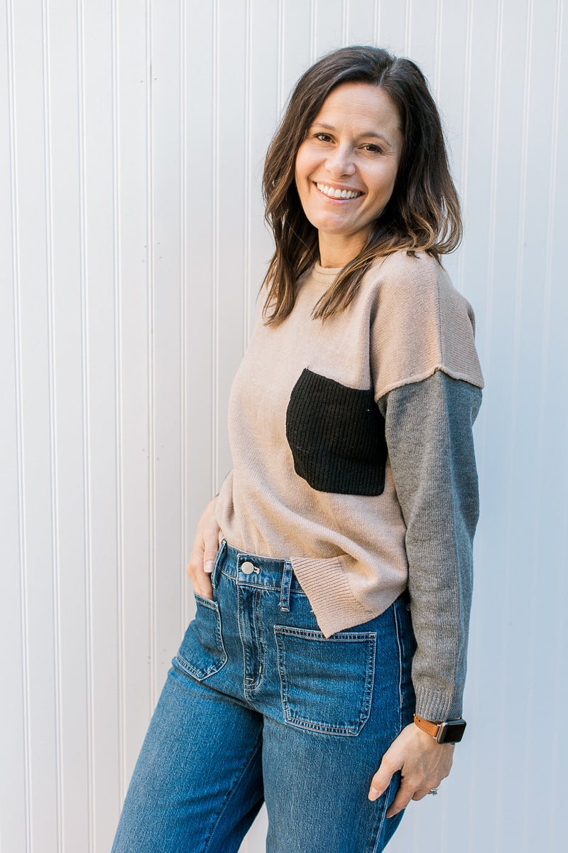 Model wearing a camel sweater with gray sleeves with exposed hem at sleeve. 