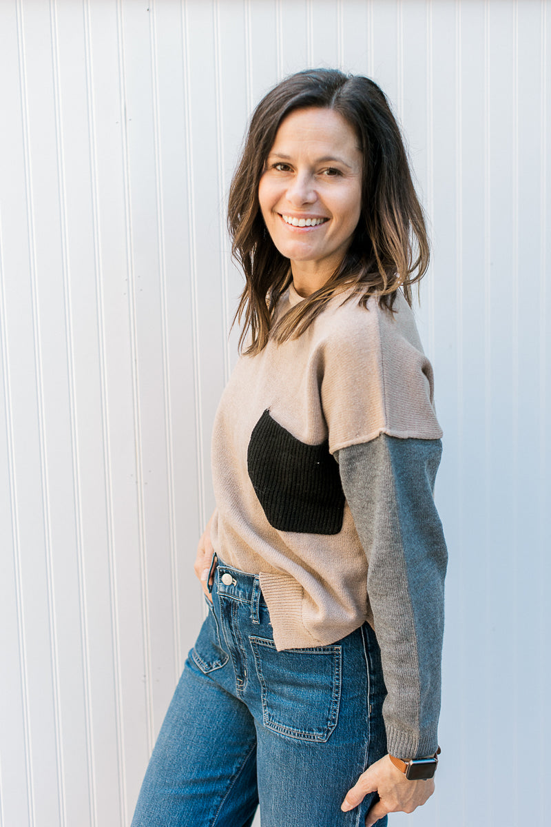 Side view of Model wearing a camel sweater with gray sleeves and a black patch pocket. 