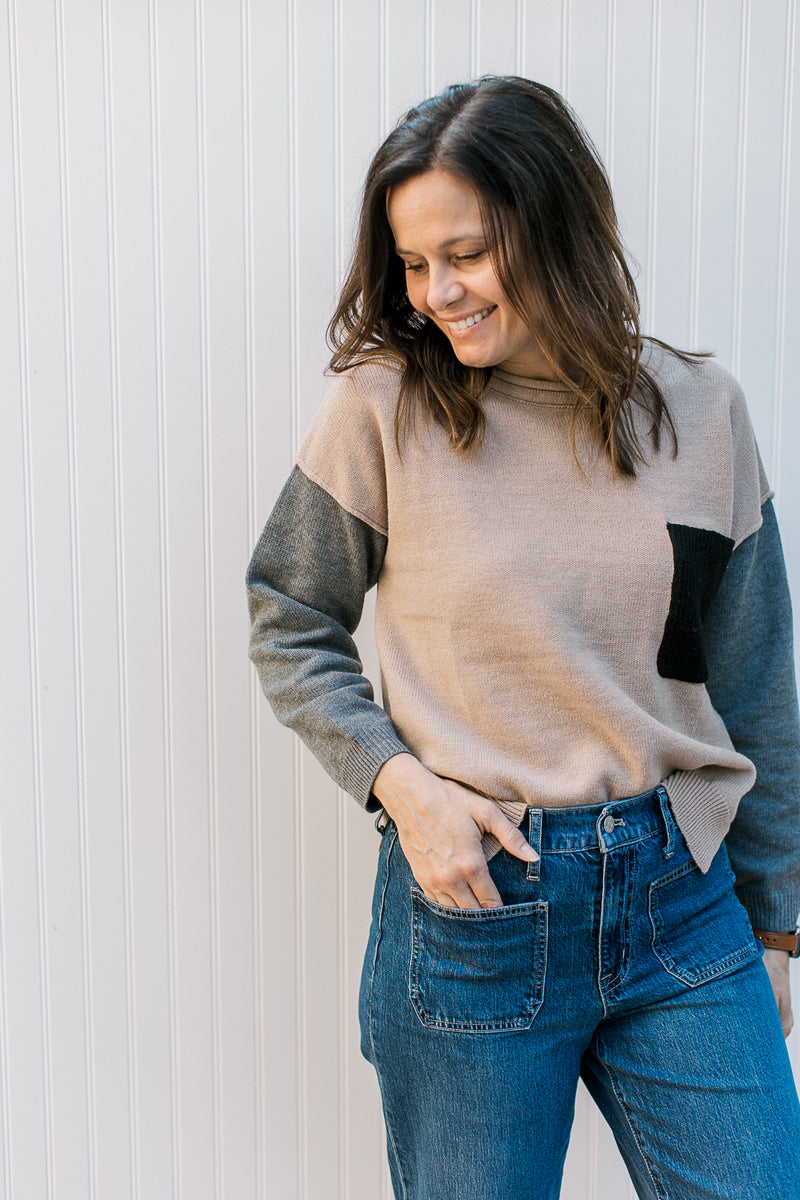 Model wearing jeans with a camel sweater with gray sleeves and a black patch pocket. 