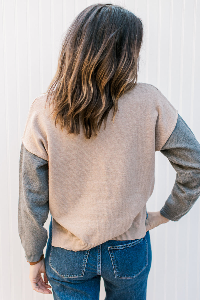 Back view of Model wearing a camel sweater with gray sleeves and a black patch pocket. 