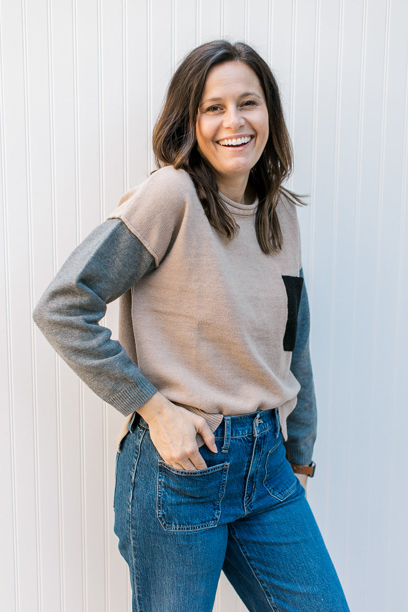 Model wearing a camel sweater with gray sleeves and a rolled neckline. 