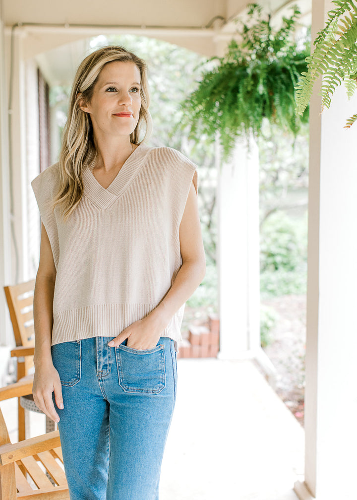 Model wearing jeans with a cream ribbed v-neck sweater with capped sleeves. 