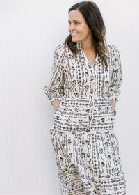 Model wearing a cream v-neck midi with a black floral design, pockets and 3/4 sleeves. 