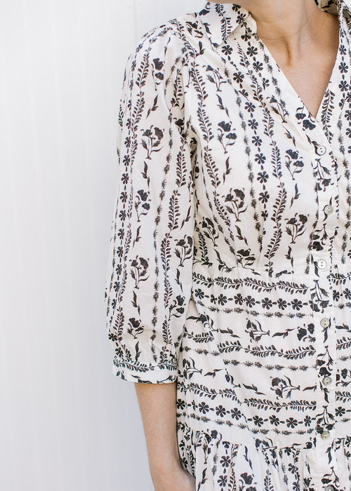 Close up of black floral design on a cream dress with a button front, collar and v-neck. 