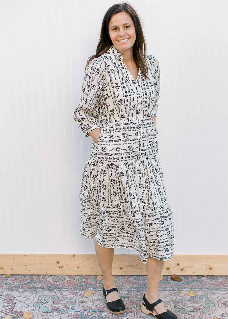 Model wearing black shoes and a cream midi with a black floral pattern and button front. 