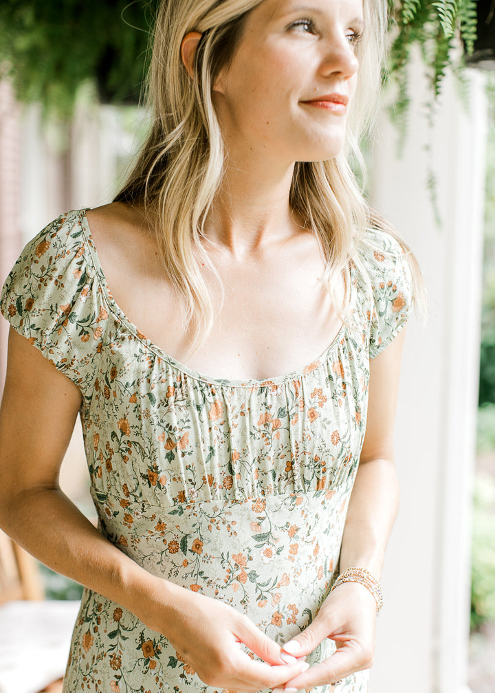 Close up on scoop neck and sort sleeves on a soft olive-green maxi with floral print. 