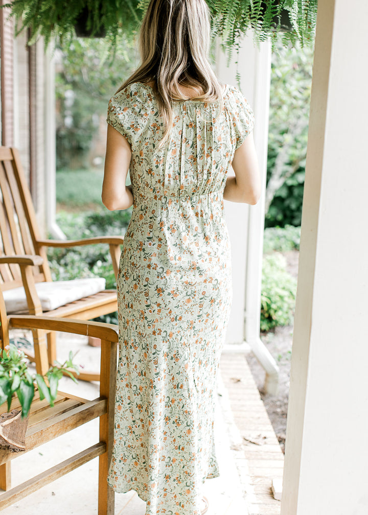 Back view of Model wearing a soft olive-green maxi with floral print, round neck and short sleeves. 