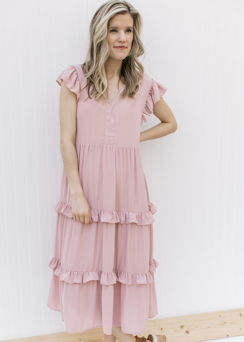 Model is wearing a blush colored midi with ruffled tiers and ruffle cap sleeves.
