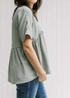 Side view of Model wearing a sage top with a babydoll fit, polyester material and short sleeves. 