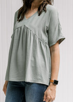 Model wearing jeans with a sage top with a babydoll fit, polyester material and short sleeves. 