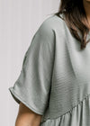 Close up view of short sleeve on a sage top with a babydoll fit and polyester material.