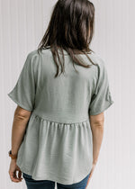 Back view of Model wearing a sage top with a babydoll fit, polyester material and short sleeves. 