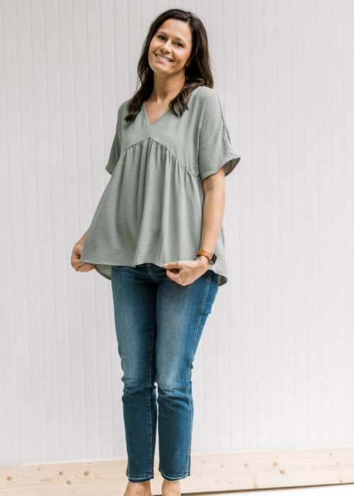 Model wearing a sage v-neck top with a babydoll fit, polyester material and short sleeves. 