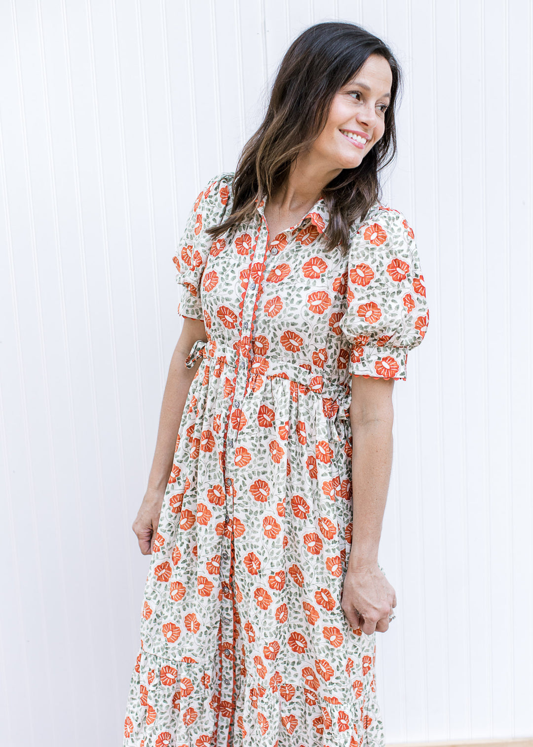 Model wearing a cream maxi with rust and green floral, scallop detail, short sleeves and side ties. 