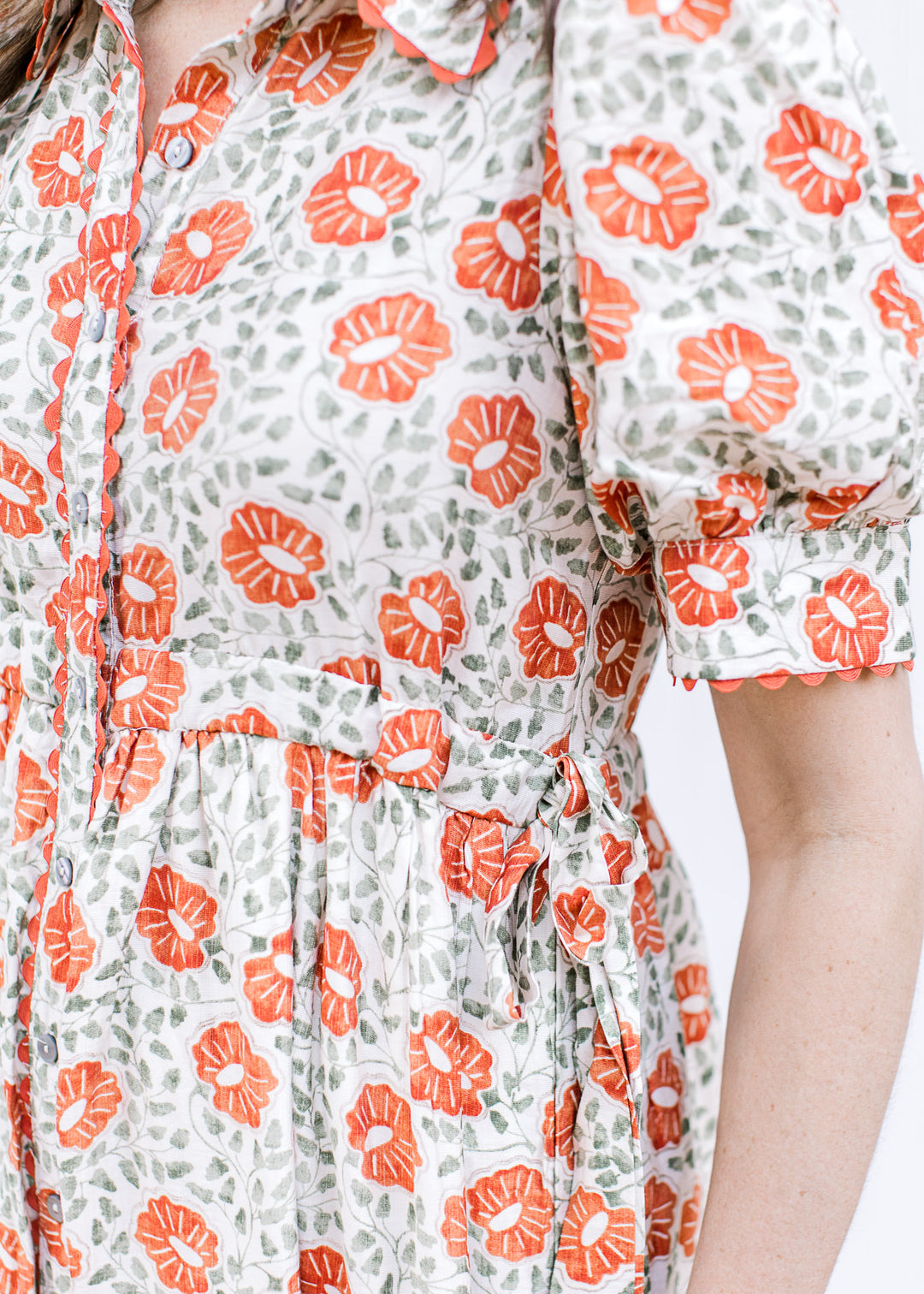 Close up of side ties and scalloping detail on a cream button up maxi with rust floral design. 
