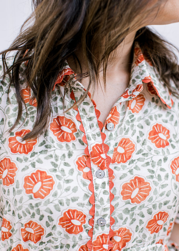 Close up of buttons and collar on a cream maxi with scalloping  detail and rust and green floral. 