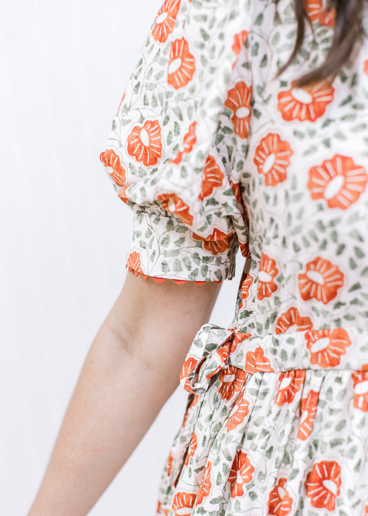 Close up of bubble short sleeves and side ties on a cream maxi with rust and green floral design. 