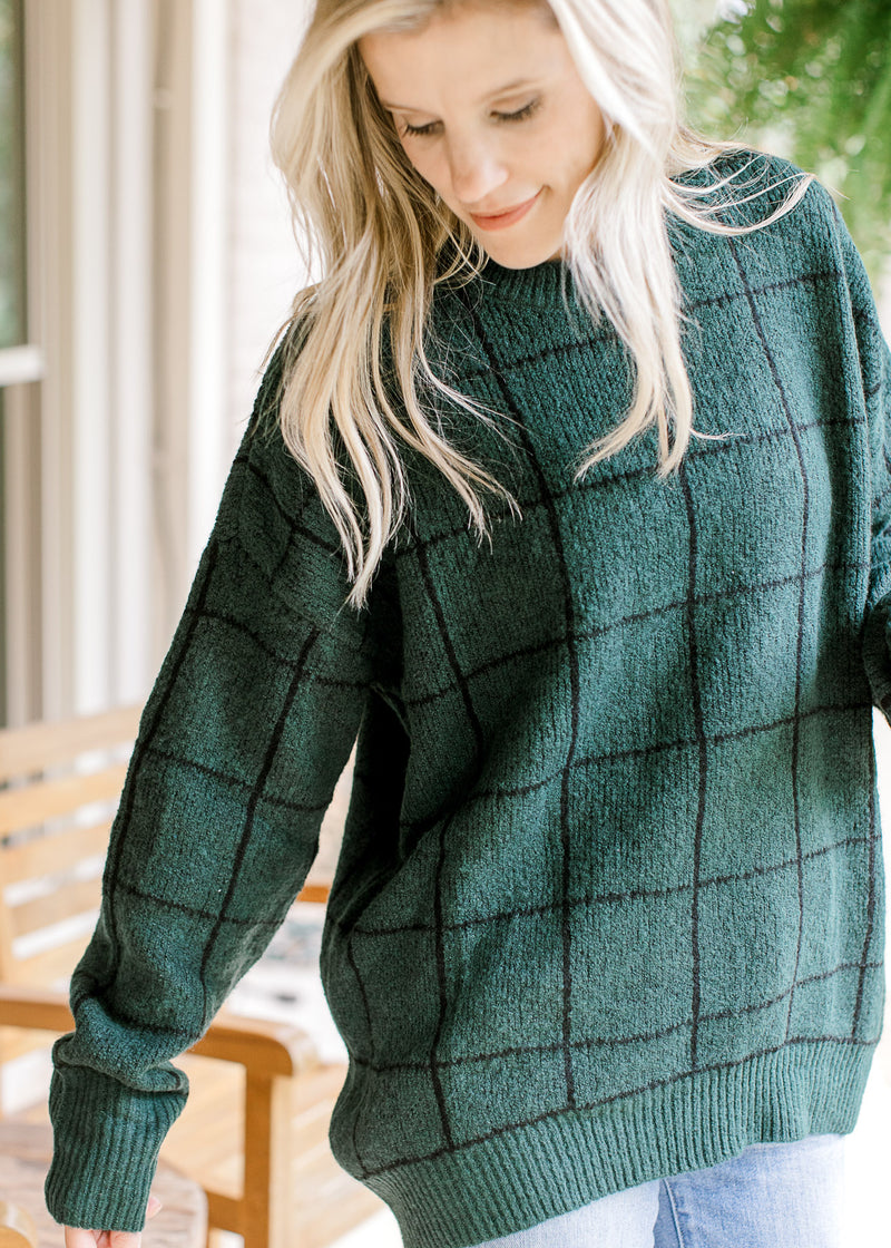 Model wearing a hunter green sweater with black window pane pattern and a round neck.