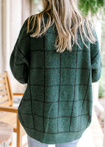 Back view of Model wearing a hunter green sweater with black window pane pattern. 