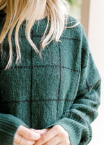 Close up of window pane pattern on an hunter green sweater with long sleeves and a round neck.