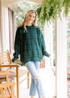 Model wearing jeans and a hunter green sweater with black window pane pattern and long sleeves. 