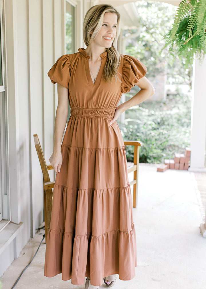 Model wearing a rust tiered maxi with an elastic waist, bubble short sleeves and a v-neck.