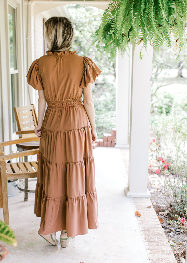 Back view of model wearing a rust maxi with tiered skirt, elastic waist and short sleeves.