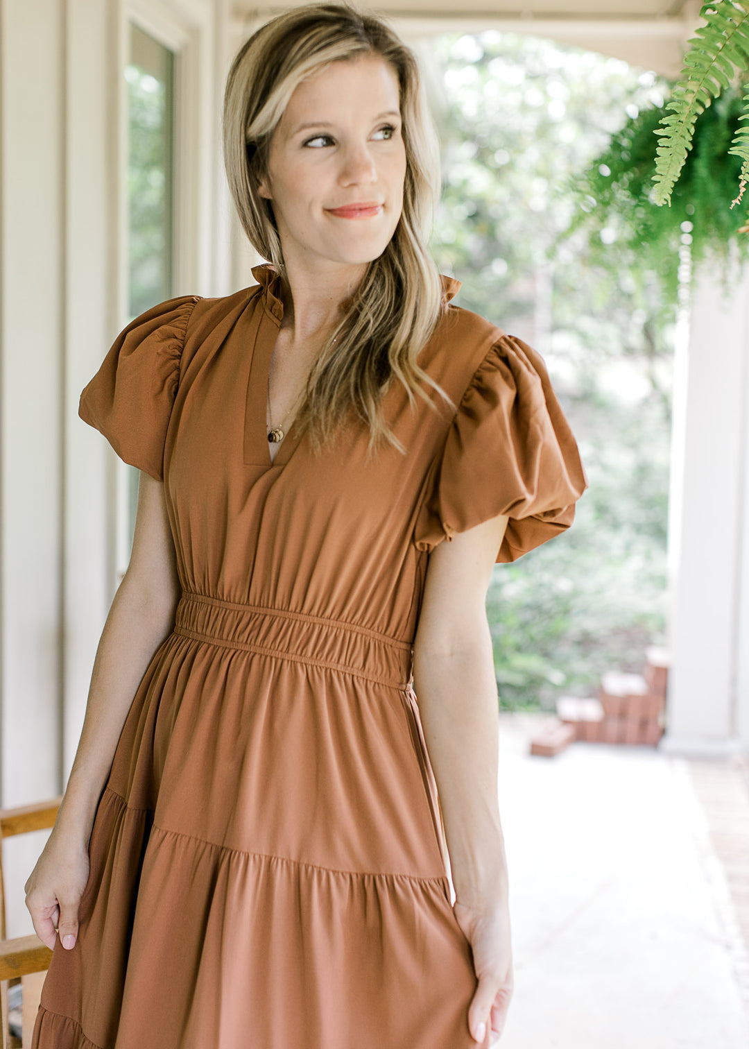Close up of model wearing a rust dress with ruffle at the neck and bubble short sleeves. 