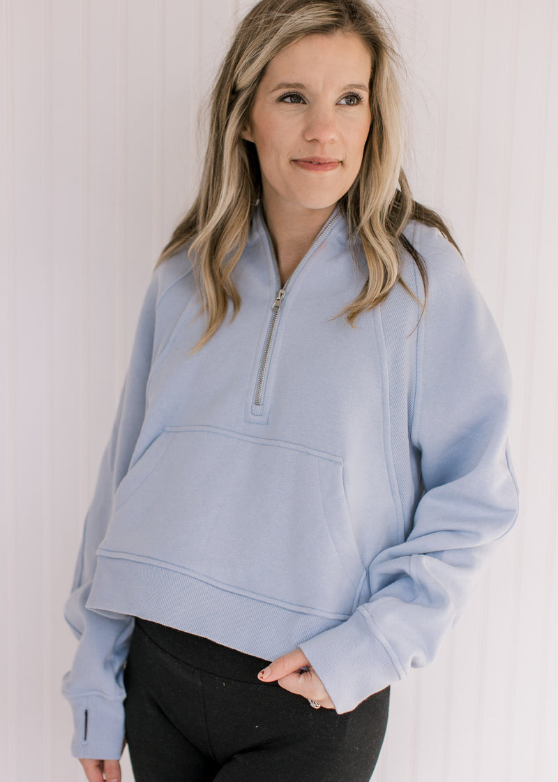 Model wearing a sky blue, slightly cropped hoodie with a 1/4 zip and long sleeves.