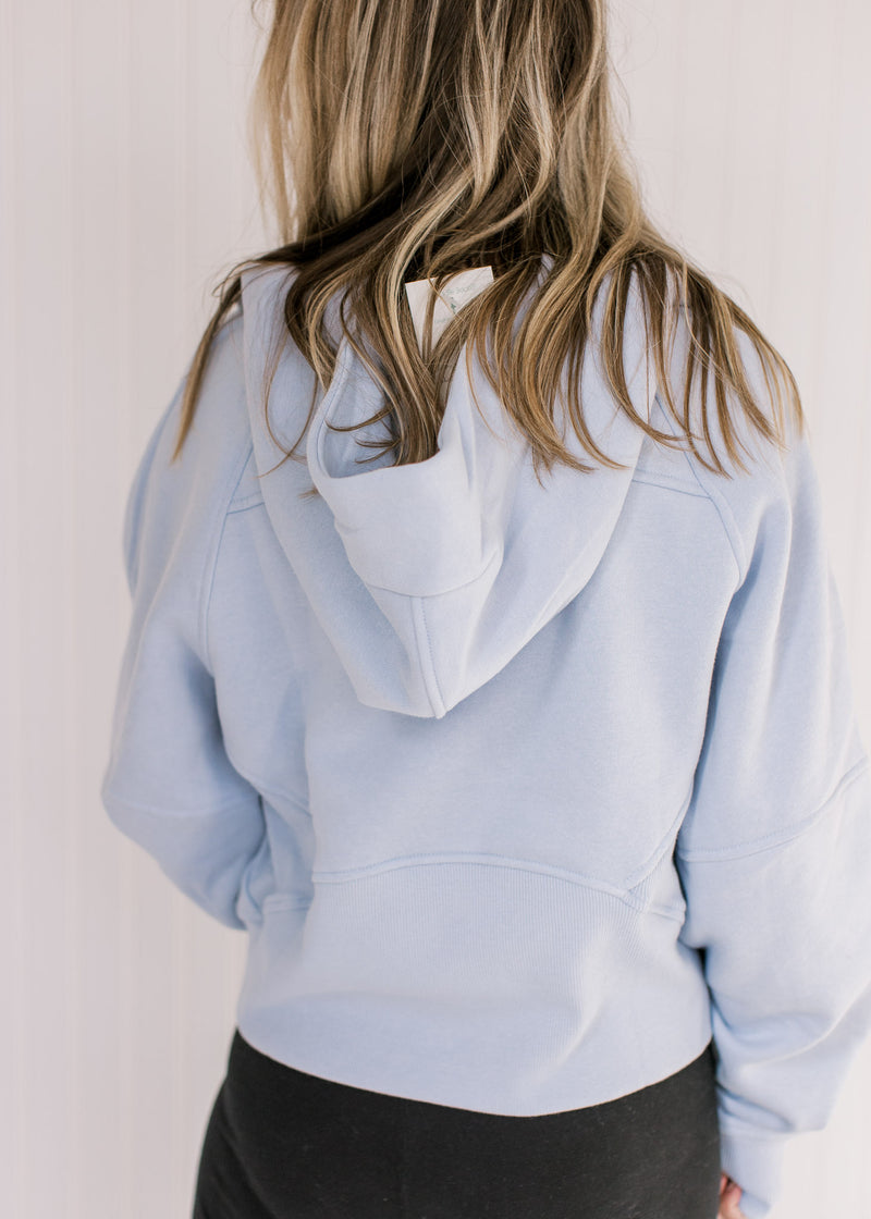 Back view of Model wearing a sky blue hoodie with a 1/4 zip, long sleeves and a front pouch pocket.