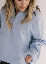 Close up of 1/4 zip and pouch pocket on a sky blue, slightly cropped hoodie with long sleeves.
