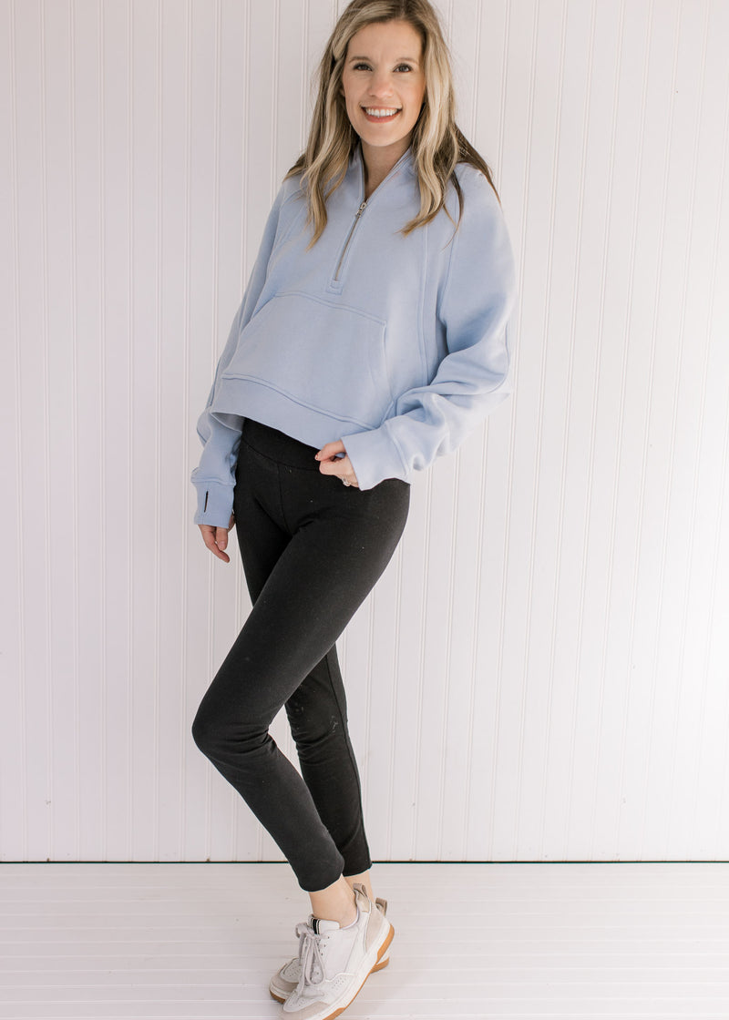 Model wearing a sky blue pullover with a 1/4 zip, long sleeves and a front pouch pocket.