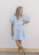 Model wearing sandals with a baby blue dress with lace lined tiers and bubble short sleeves.