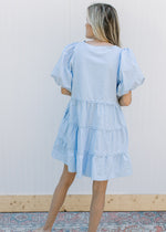 Back view of Model wearing a baby blue dress with lace lined tiers and bubble short sleeves.