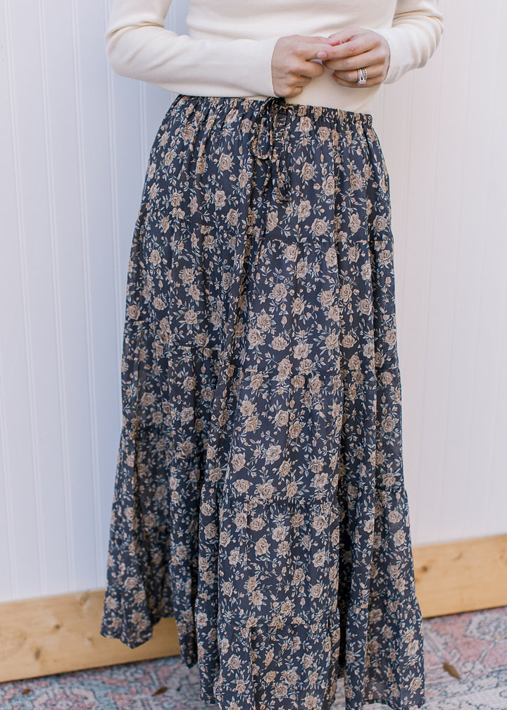 Model wearing a flowy, slate blue midi with tan floral, elastic waist with tie and pockets. 