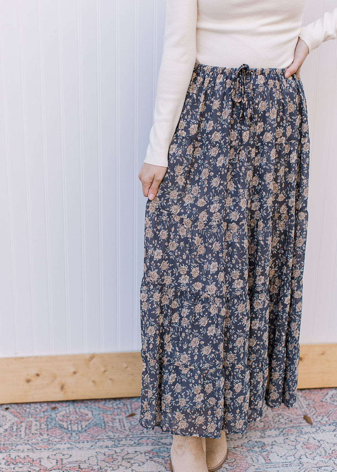 Model wearing a flowy, slate blue midi with tan floral, elastic waist with tie, tiers and pockets. 