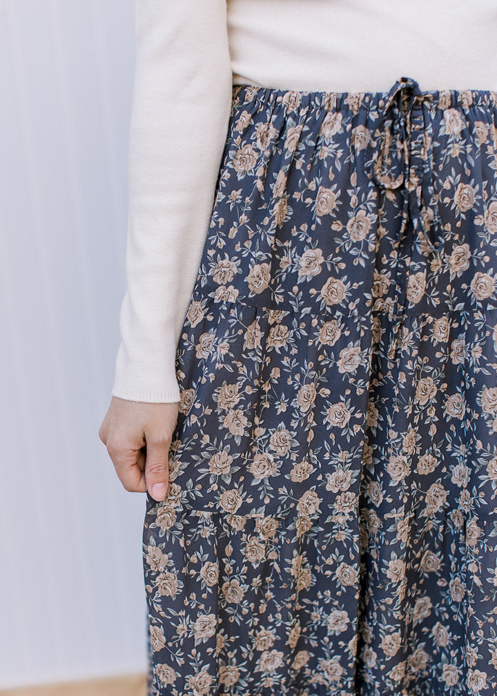 Close up of elastic band and tie on a slate blue midi with tan floral, tiers and a flowy fit. 