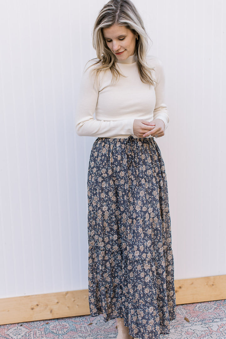  Model wearing a cream top and a slate blue midi with floral, elastic waist with tie and pockets. 