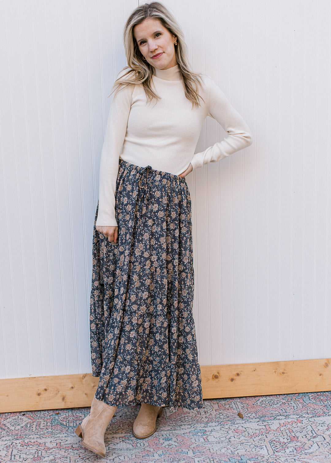 Model wearing boots, cream fitted top and a slate blue midi with floral and elastic waist with tie. 