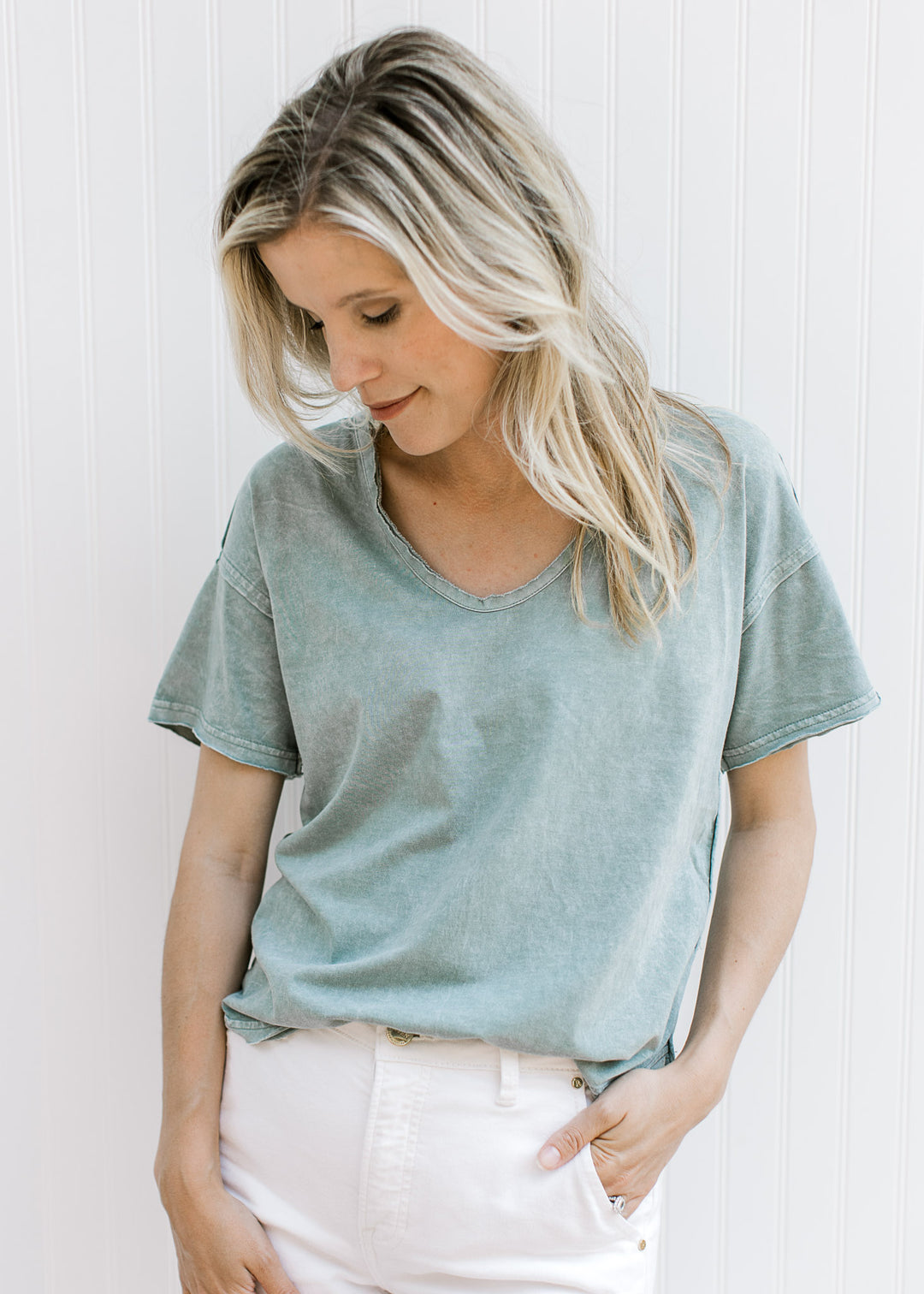Model wearing a cotton slate blue top with a v- neck, short sleeves and a raw hemline.